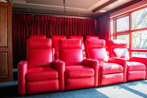 Elegant home theater featuring vibrant red leather reclining chairs and natural light.